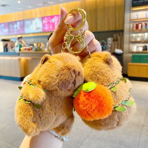 Two cute capybara plush keychain charms, one shown from the front and the other wearing an orange fruit backpack.