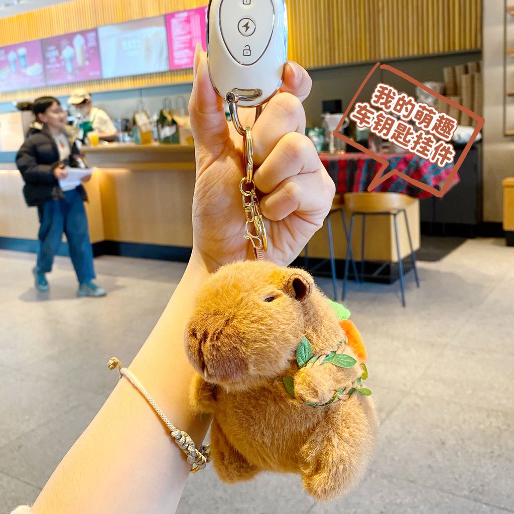 Cute capybara plush keychain with orange fruit backpack attached to a car key fob