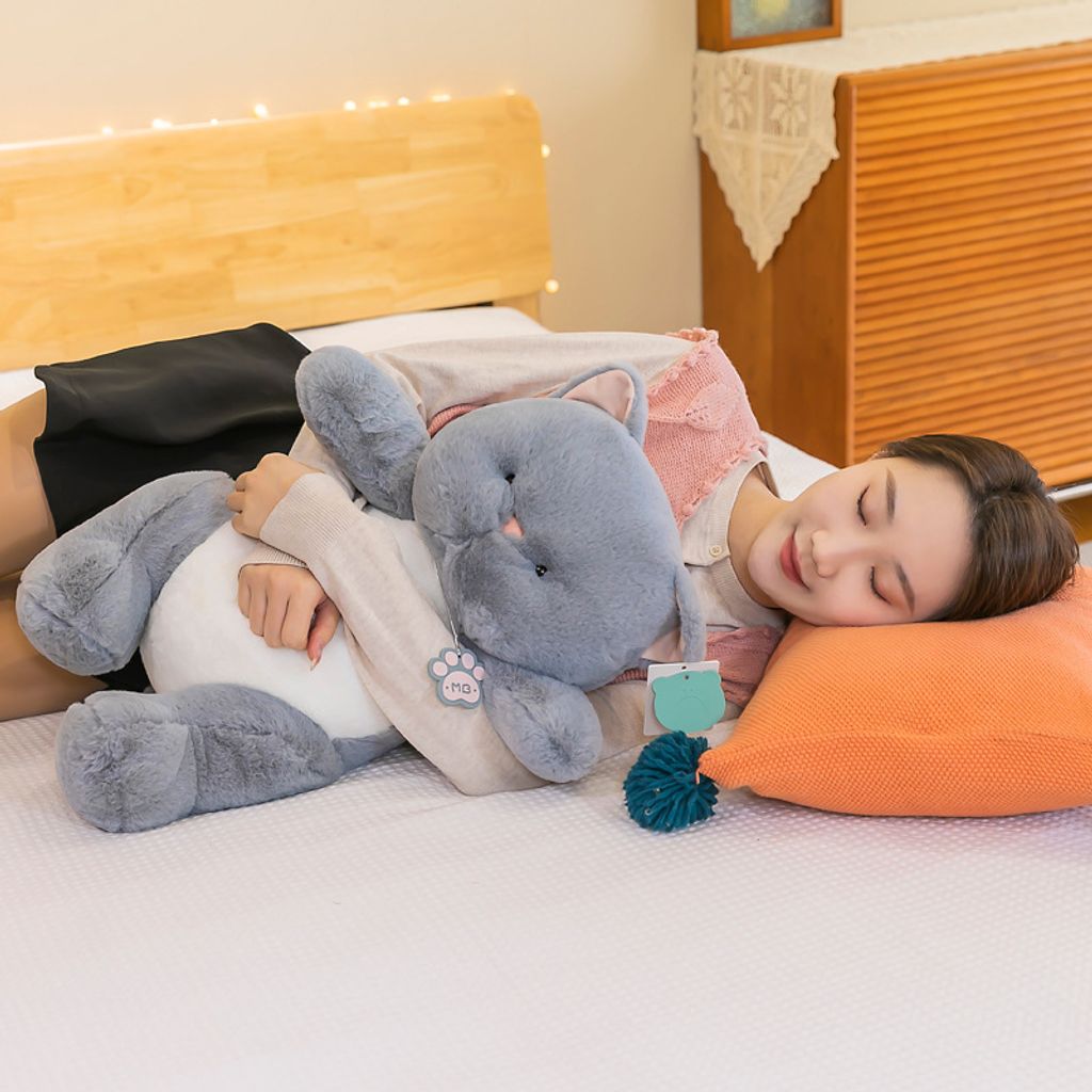 Gray cat plush toy used as a hugging pillow while resting on a bed