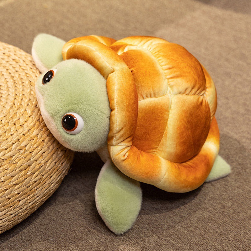 Bread turtle plush toy leaning on a woven mat, featuring a fluffy green face and bread-shaped shell