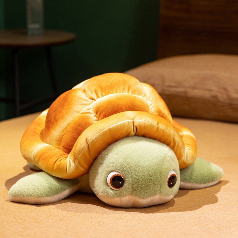 Bread turtle plush toy lying on a bed, featuring a soft golden bread shell and green flippers