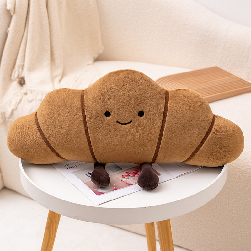 Croissant bread plush pillow with curved shape and soft fabric on a round table