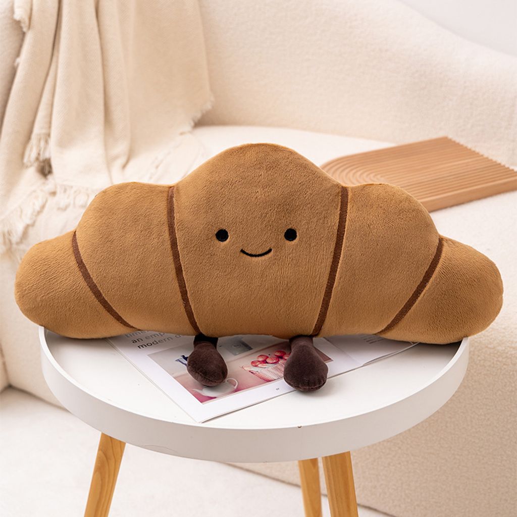Croissant bread plush pillow with curved shape and soft fabric on a round table