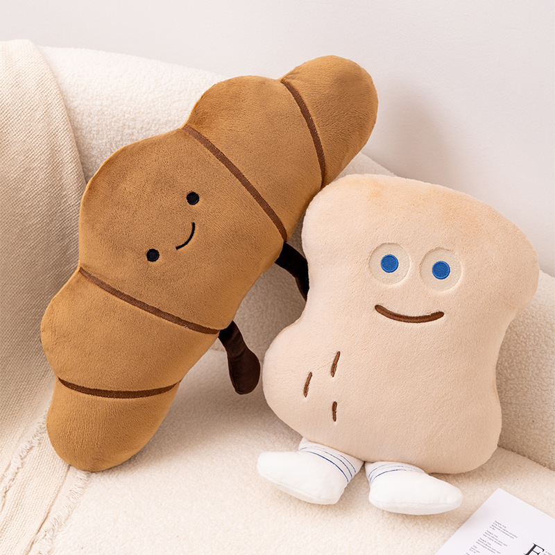 Croissant and Peanut Bun plush pillows leaning together on a cozy sofa
