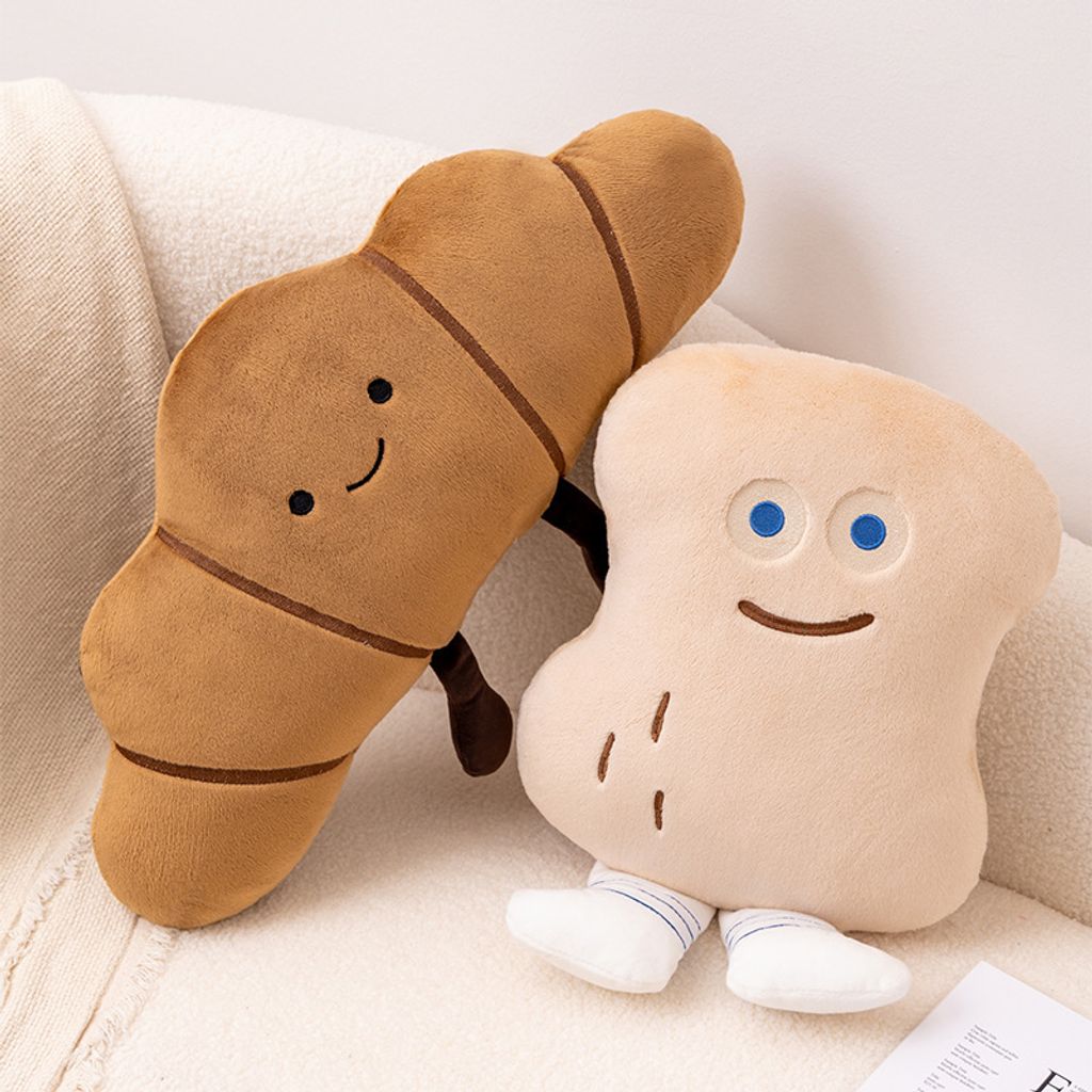 Croissant and Peanut Bun plush pillows leaning together on a cozy sofa