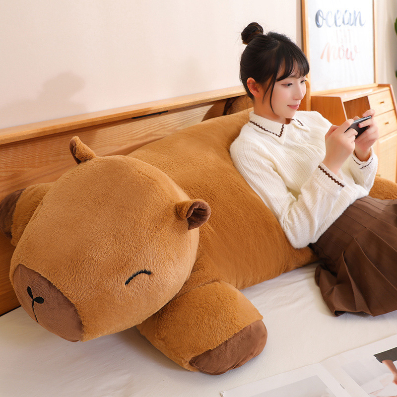 Capybara plush cushion used as a soft backrest pillow on a bed for relaxing and lounging