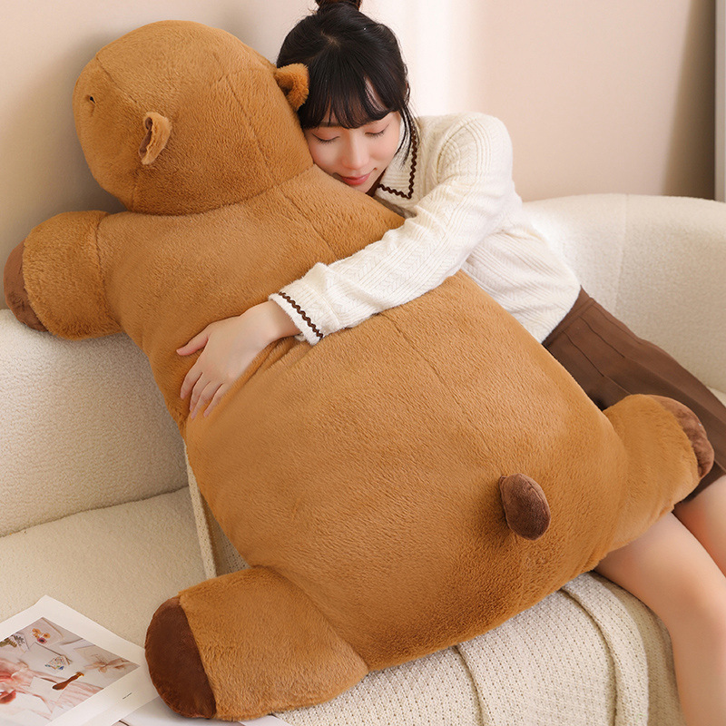Capybara plush cushion used as a large hugging pillow for relaxing on a sofa in a cozy home setting