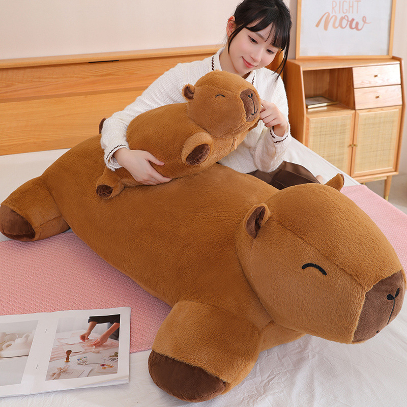 Capybara plush cushion held to show size comparison, soft texture, and cozy hugging comfort on a bed