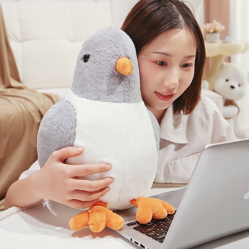 Gray pigeon plush toy sitting on a laptop, showing soft texture and cozy desk companion use