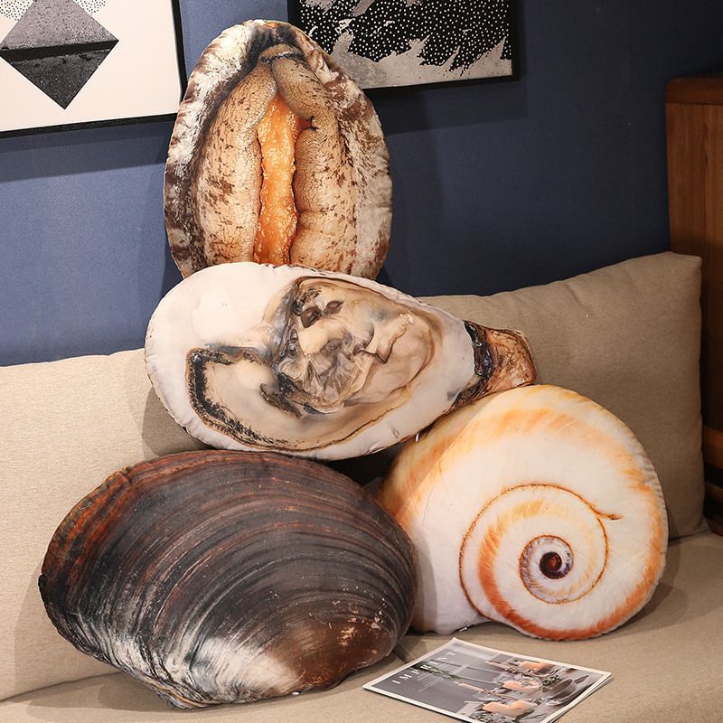 Realistic seashell plush pillows displayed on a sofa, including conch shell, oyster, abalone, and mussel designs, adding a relaxed ocean-themed decorative touch to living spaces