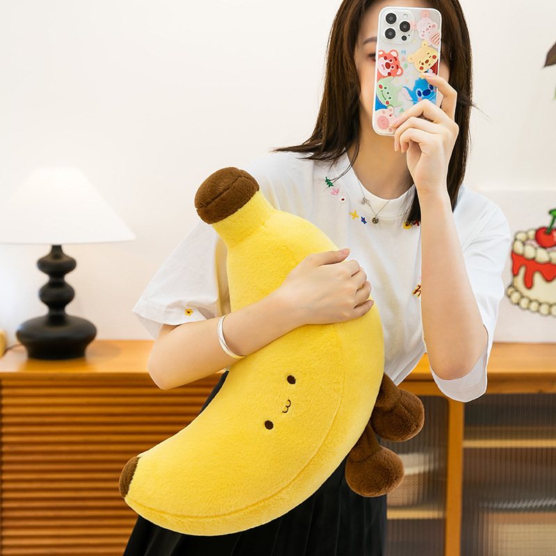 Large banana plush toy with legs hugged close, soft and fluffy cuddle plush used as comfort pillow for relaxing and cozy indoor moments