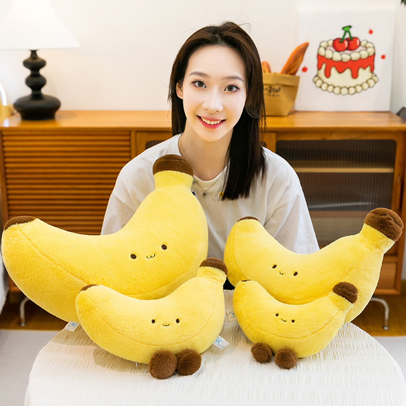 Banana plush toy with legs displayed in multiple sizes on a table, soft yellow plush design ideal for hugging, gifting, and cute home decor
