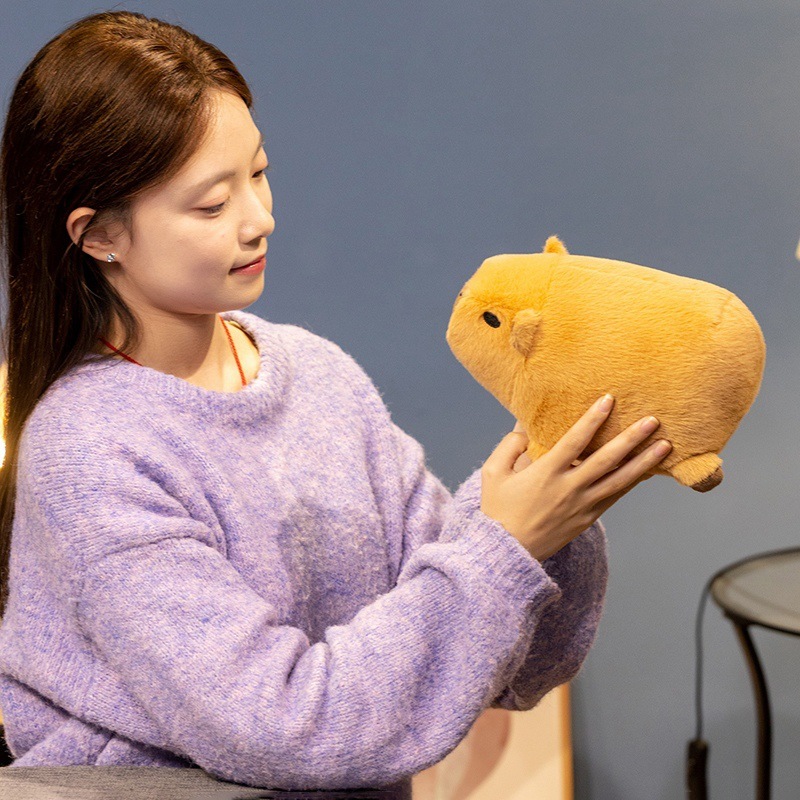 Capybara plush toy held for size reference, soft and rounded stuffed animal with a cozy feel, ideal for hugging, relaxing, and cute home decor