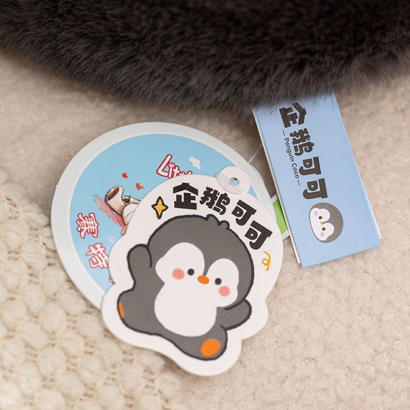 Coco Penguin plush toy brand tag detail, close up of product label and character tag attached to soft penguin stuffed toy, showing branding and cute design details