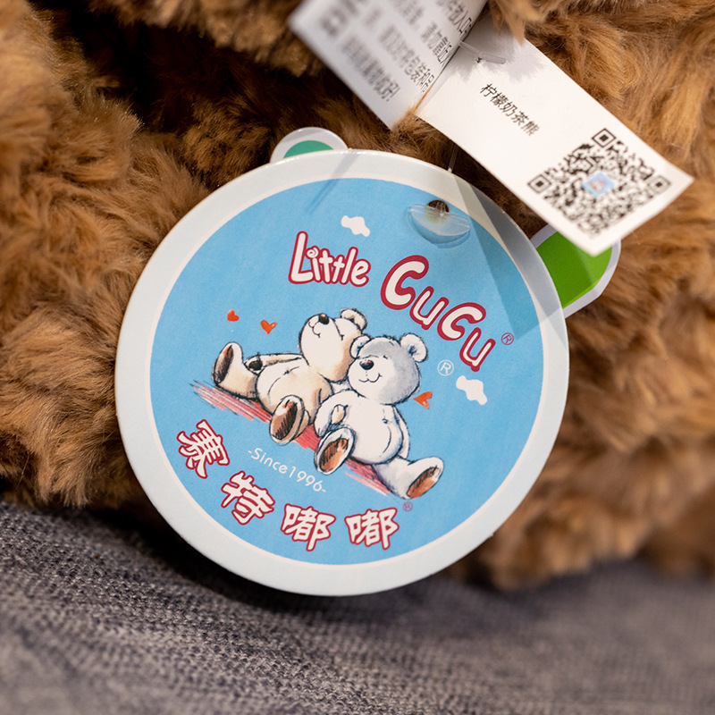 Detail view of milk tea bear plush toy tag, showing brand hang tag and fabric label attached to the plush toy