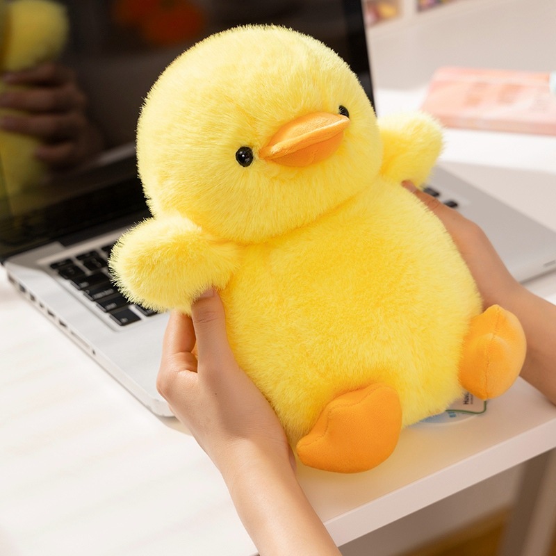 Yellow duck plush toy with soft fluffy texture, compact size for easy hugging, placed on a desk as a cute companion for work or study, adding warmth and cozy vibes to everyday spaces