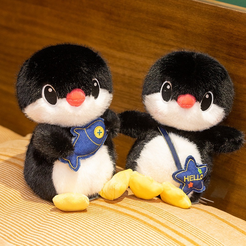 Two penguin plush toys with fish and backpack designs displayed together on a sofa, highlighting different styles