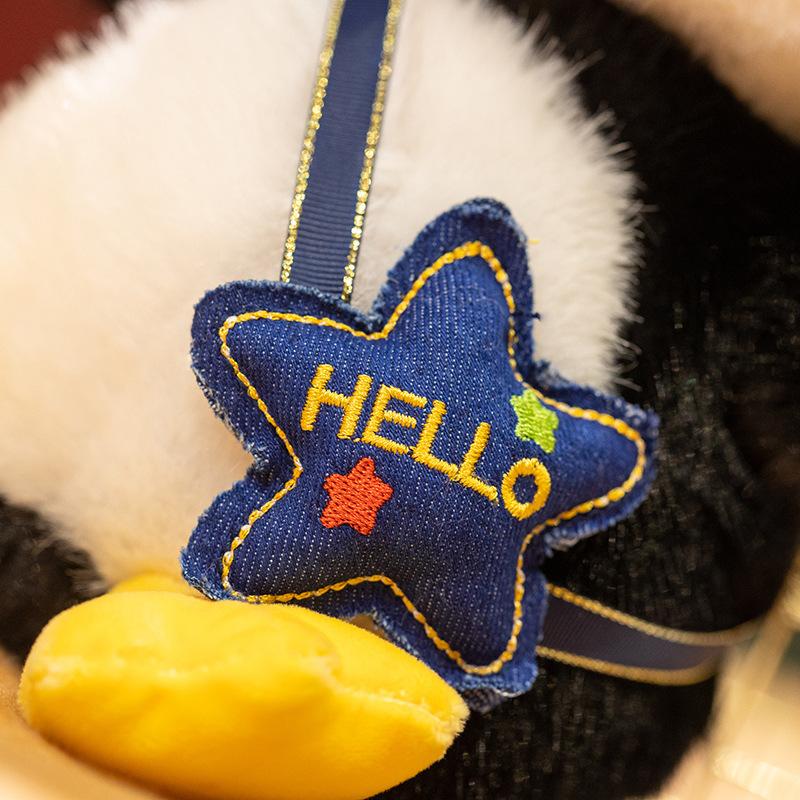 Penguin plush toy backpack detail with star shaped pouch and stitched hello design