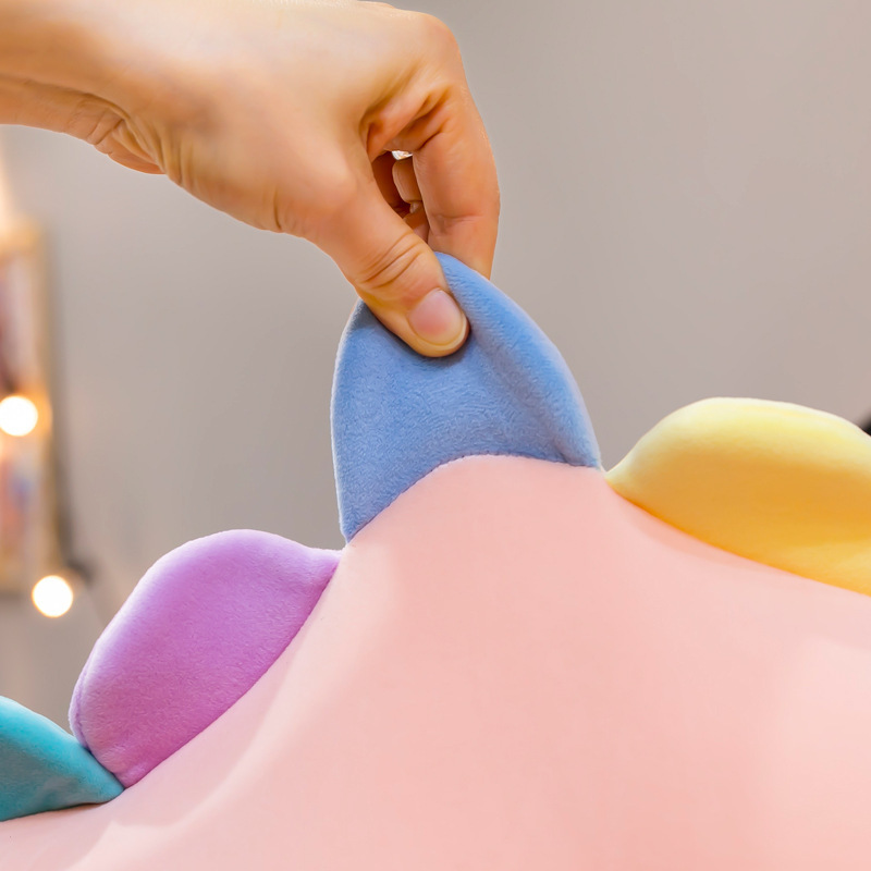 Candy dinosaur plush toy back detail showing soft pastel padded spikes being gently compressed, highlighting plush fabric texture, elasticity, and comfortable cushioning in a cozy indoor setting