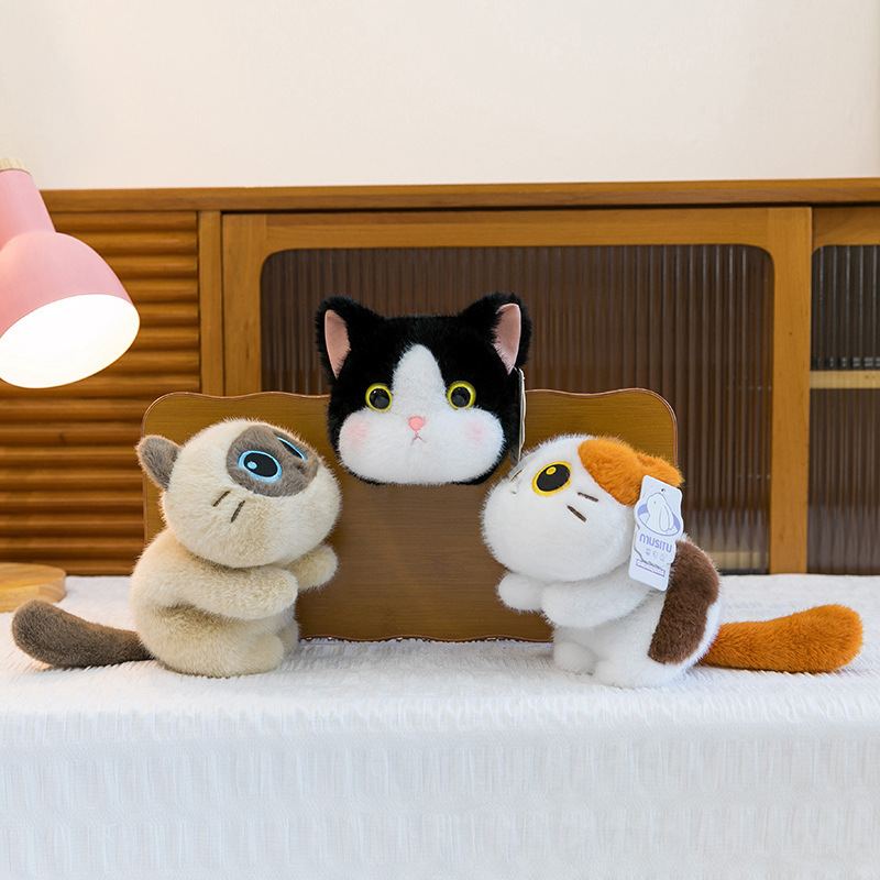 Three soft lying cat plush toys displayed together on a cozy surface, showcasing different colors and designs, with a fluffy texture and playful pose for warm home decor and comforting companionship