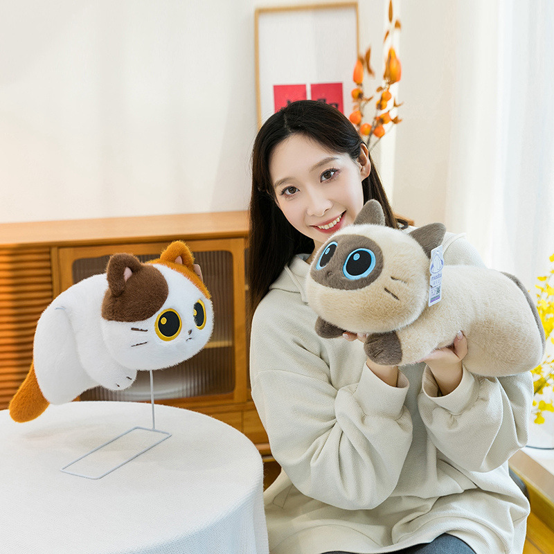 Soft lying cat plush toy displayed in a cozy home setting, showing two color variants with a rounded body, short legs, and smooth plush fabric, suitable for hugging, relaxing, or decorative display on tables and shelves
