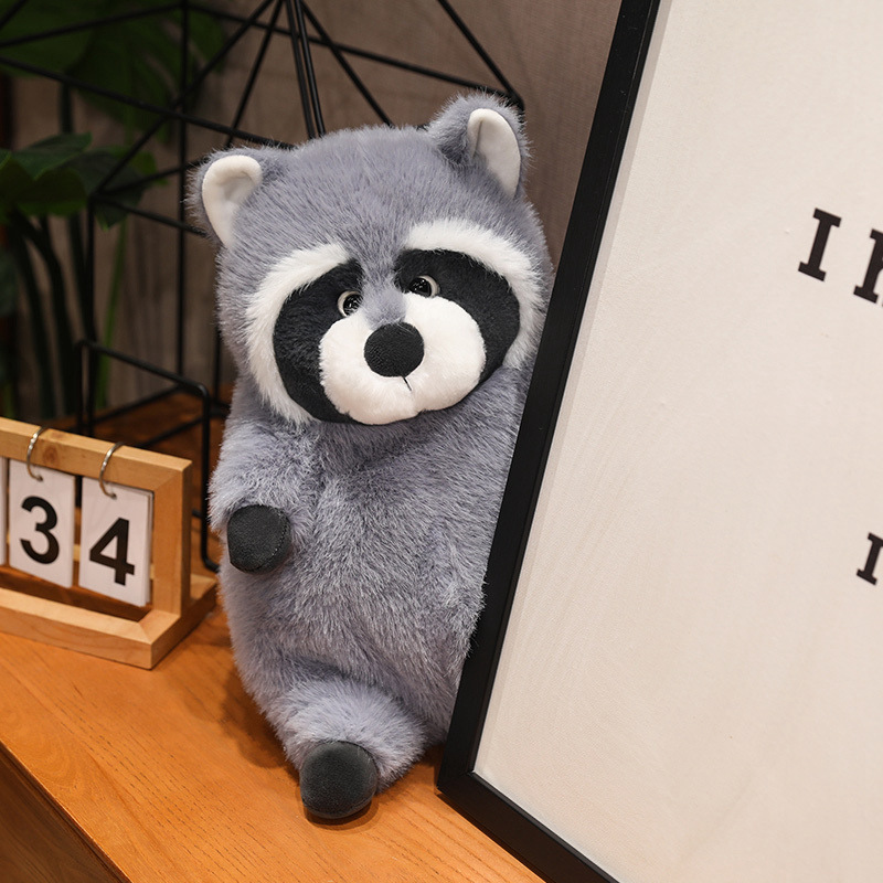 Chubby raccoon plush toy leaning against a decorative frame on a wooden surface, highlighting its soft plush fabric and rounded design, perfect for shelf styling, room decor, and a cozy home display