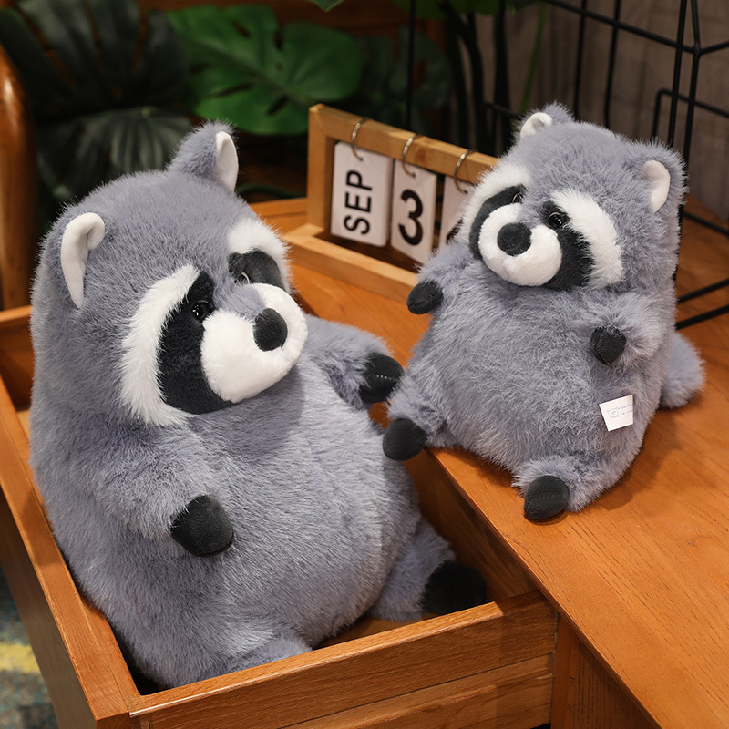 Chubby raccoon plush toy displayed on a wooden drawer and table, showing soft fluffy texture, rounded shape, and cozy home decor styling for shelves, desks, or bedside spaces