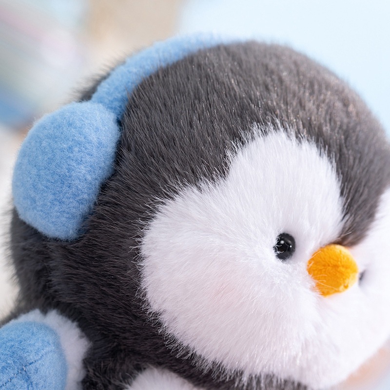Close-up of coco standing penguin plush toy with blue ear muffs, showing soft plush fabric, fluffy texture and fine stitching for a cozy and comforting feel