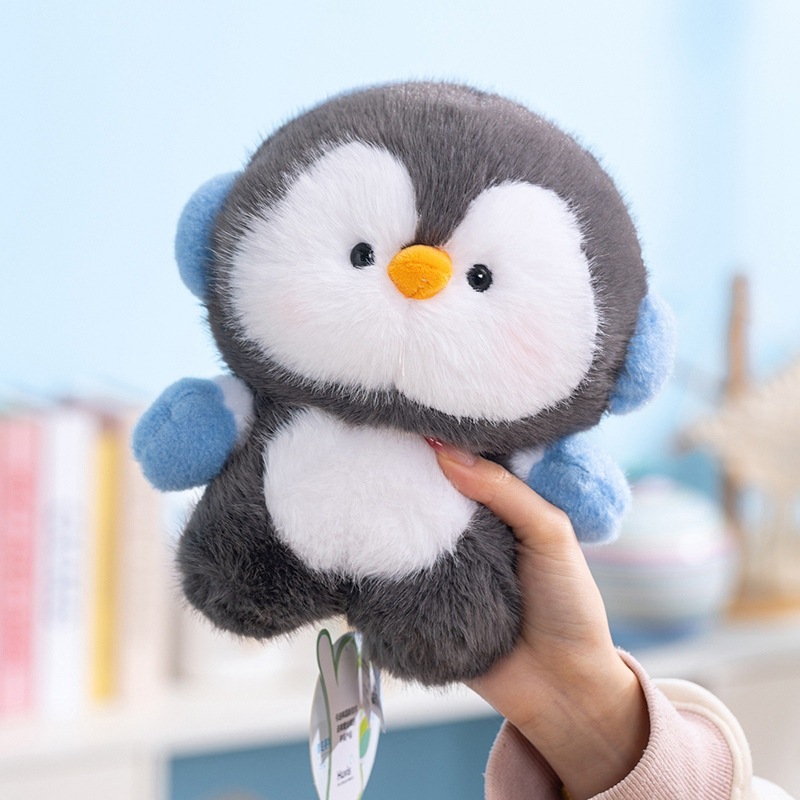 Coco standing penguin plush toy with blue ear muffs, round fluffy body and soft plush fabric, warm winter themed stuffed animal for display, hugging, and cozy home decor