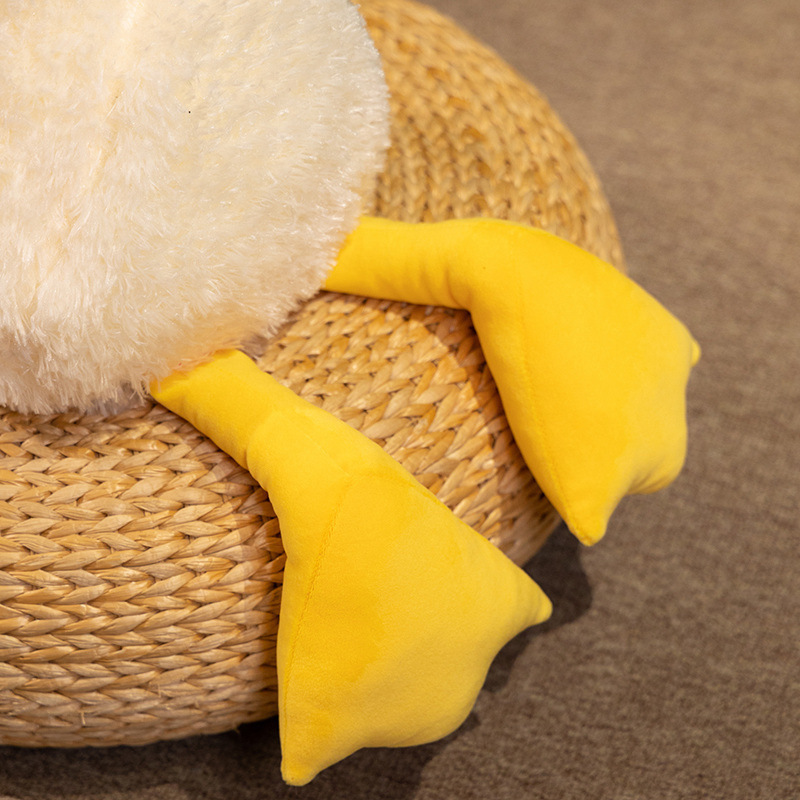Detail view of the lying white duck plush pillow showing soft yellow feet and plush body, designed for cozy hugging and lounging