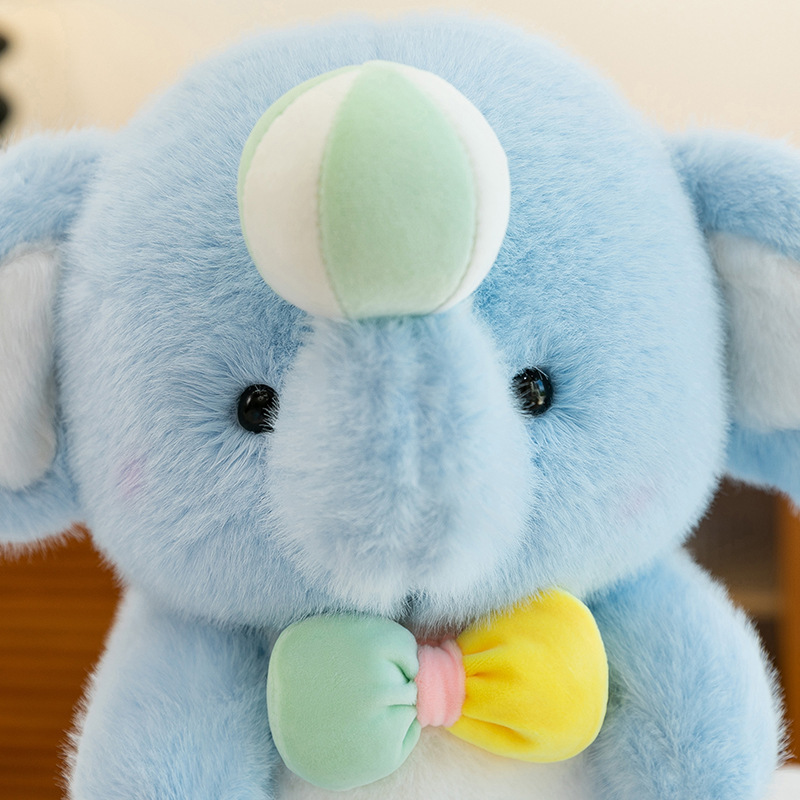 Close-up of blue happy elephant plush toy with soft fluffy texture, rounded snout, black safety eyes, pastel bow accent, and a gentle, comforting design