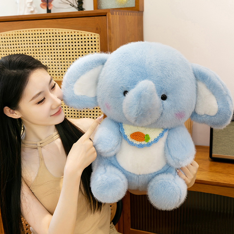 Happy elephant plush toy with bib detail and black safety eyes, displayed in a warm indoor environment to show its size, fluffy body, and cuddly companion feel
