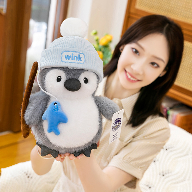 Fishing penguin plush toy with blue knit hat and fish detail, cute chubby design made for hugging, gifting, and cozy room decoration