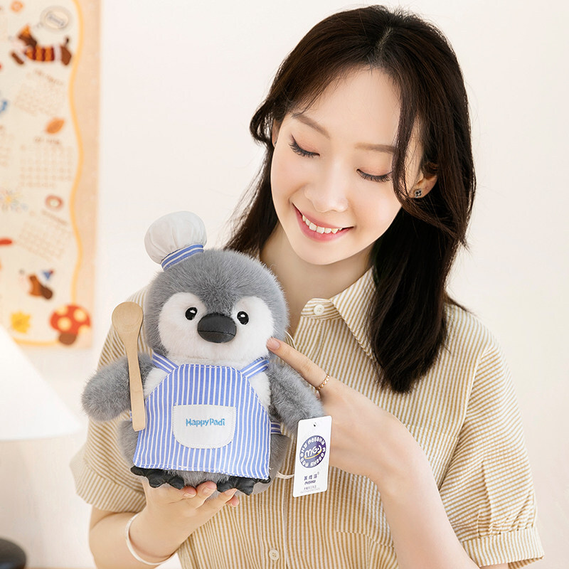 Chef penguin plush toy in blue striped apron with soft plush texture, compact size for easy holding, cozy and cute design ideal for gifting or shelf decor