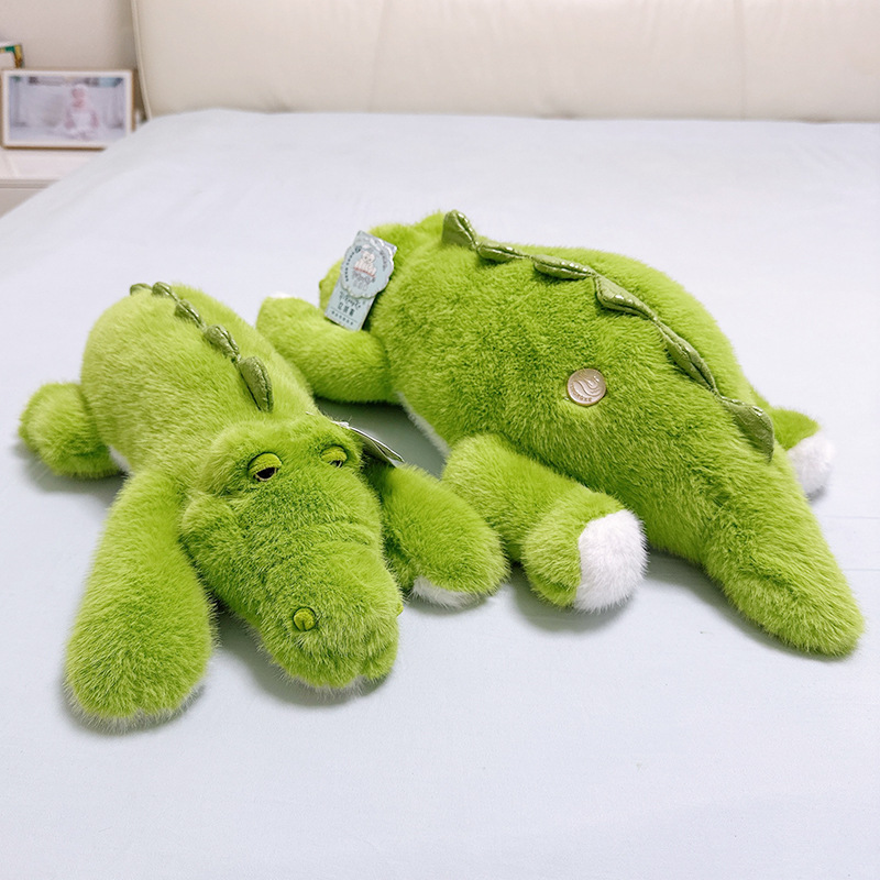 Two green lying crocodile plush toys placed front and back on a bed showing soft stuffed alligator design