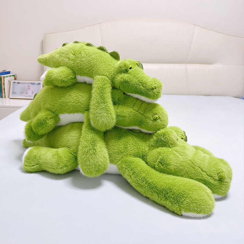 Green lying crocodile plush toys in different sizes stacked on bed