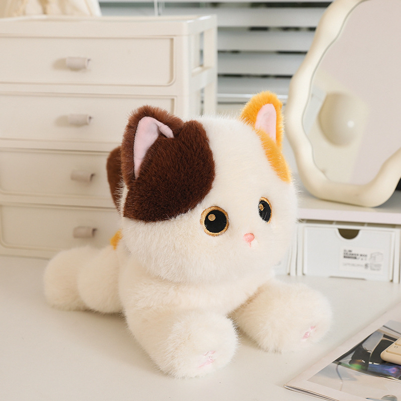 Calico poseable cat plush toy in lying pose displayed on a desk surface, soft fluffy texture with detailed facial features in a cozy indoor setting