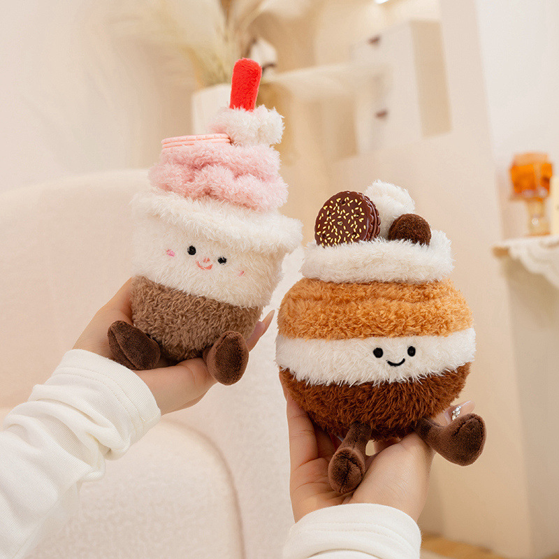 Cute dessert plush toys including cupcake and macaron cake designs with fluffy plush fabric, embroidered faces and sweet pastel colors, styled in a warm indoor decor setting
