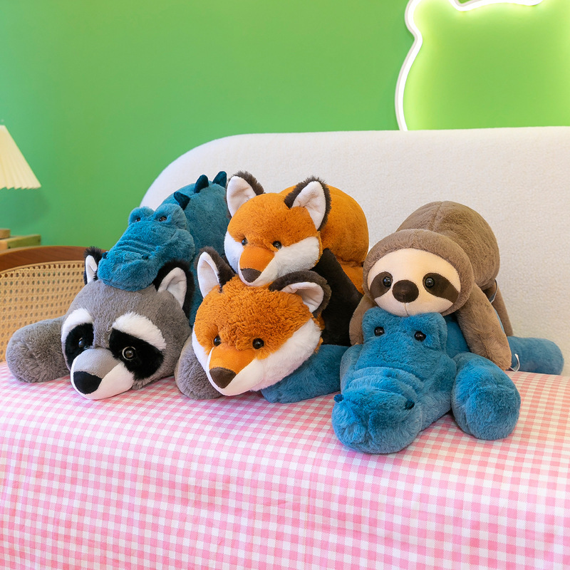 Lazy lying animal plush toys stacked together on a bed, crocodile, raccoon, fox and sloth designs in soft plush fabric for comfort, gifting and cozy home styling