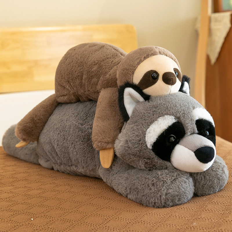 Sloth and raccoon lazy lying plush toys stacked together on a bed, soft stuffed animal pillows for cuddling and cozy home decor