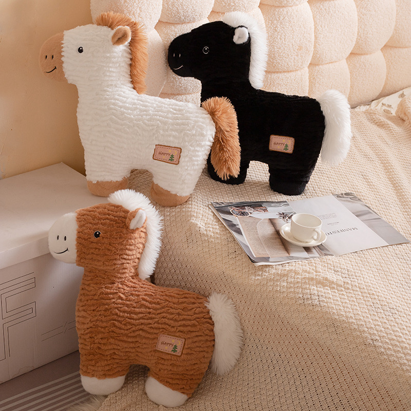 White, black, and brown horse plush pillows arranged on a bed and knitted blanket, highlighting soft plush texture, fluffy tails, and warm cozy home decor atmosphere