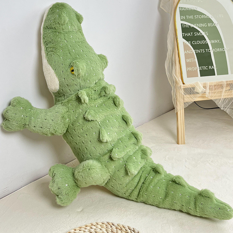 Green crocodile plush toy with long body and textured back scales leaning against wall in cozy home setting