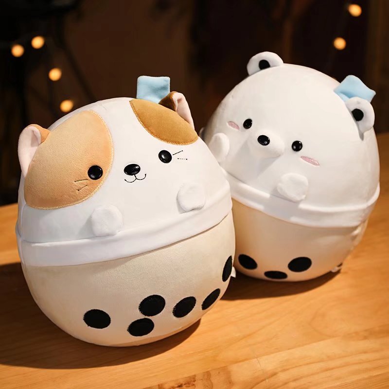 Milk tea animal plush toys featuring cat and white bear designs displayed on a wooden table, soft rounded shapes with bubble tea cup details in warm ambient lighting