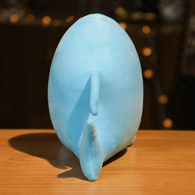 Back view of shark milk tea animal plush toy showing smooth blue plush fabric and tail detail displayed on a wooden table in warm lighting