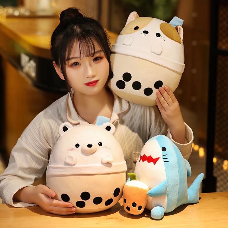 Milk tea animal plush toys featuring white bear, shark and cat designs placed on a desk, soft plush texture with cute bubble tea cup details in a warm ambient setting