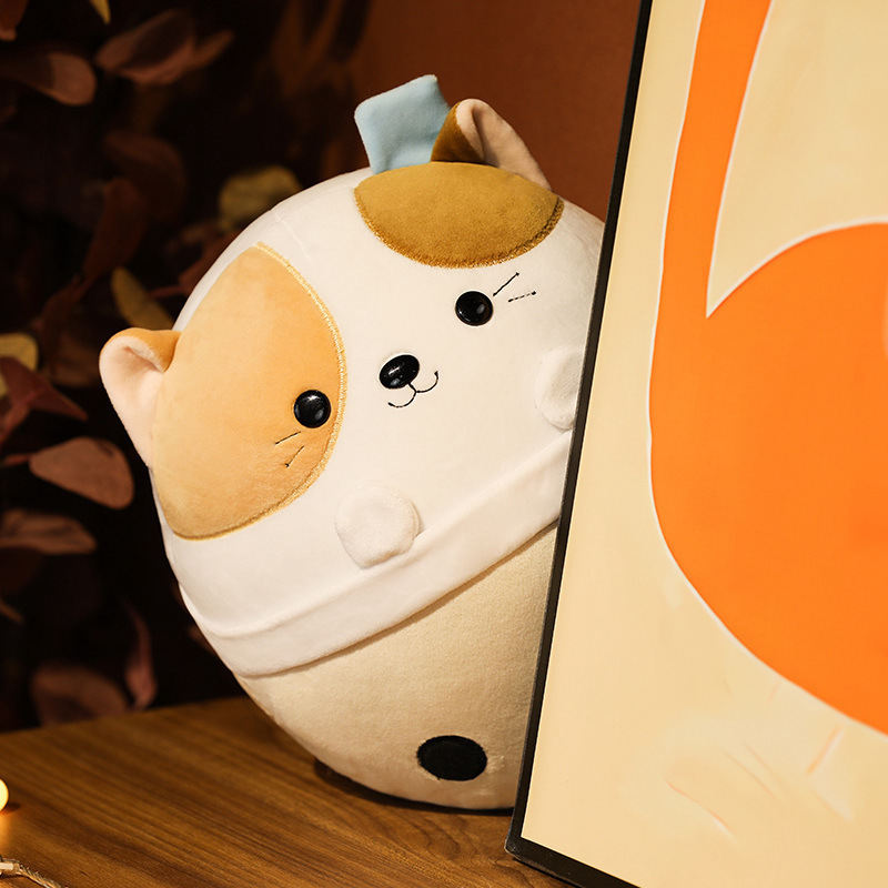 Cat milk tea animal plush toy placed on a wooden table beside a framed decor piece, soft plush texture and rounded bubble tea cup shape in a cozy indoor setting