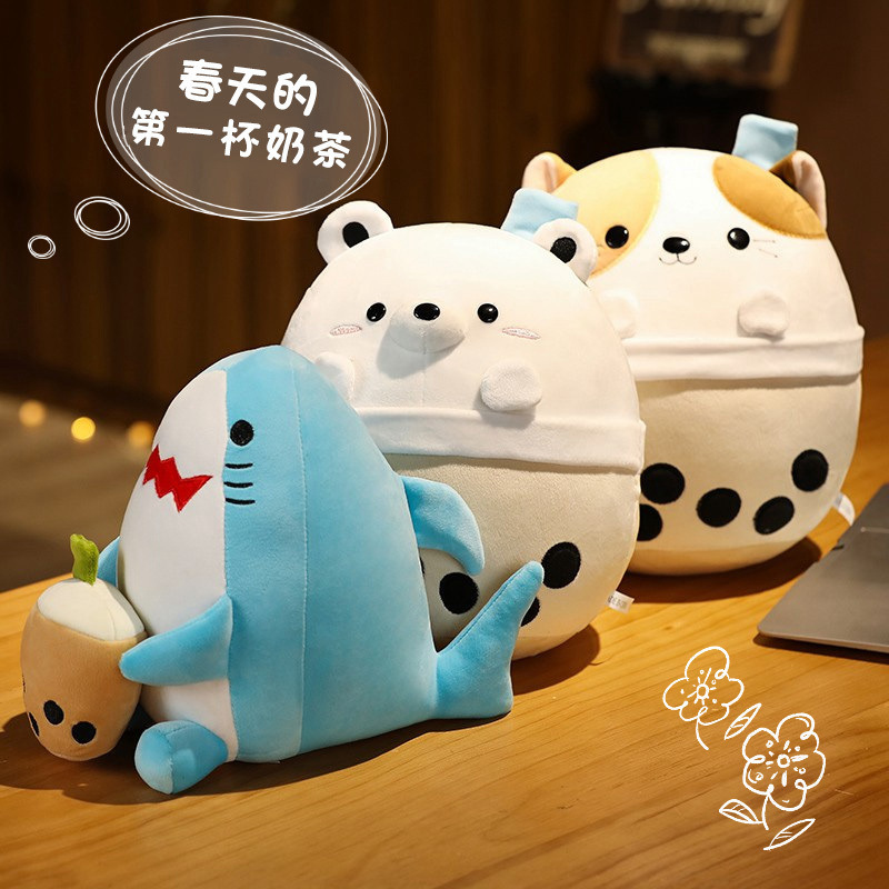 Milk tea animal plush toys in bear, cat and shark designs arranged on a wooden table, soft rounded shapes with bubble tea cup details in a warm cozy indoor setting