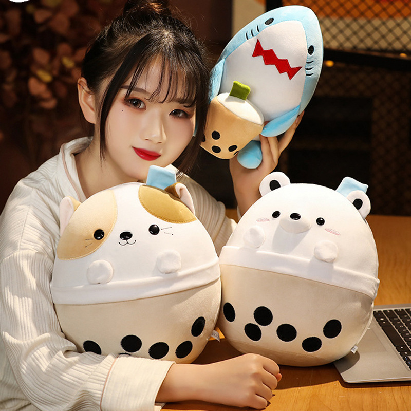 Milk tea animal plush toys in bear, cat and shark designs displayed on a wooden table, soft rounded shapes with bubble tea cup details in a cozy indoor setting