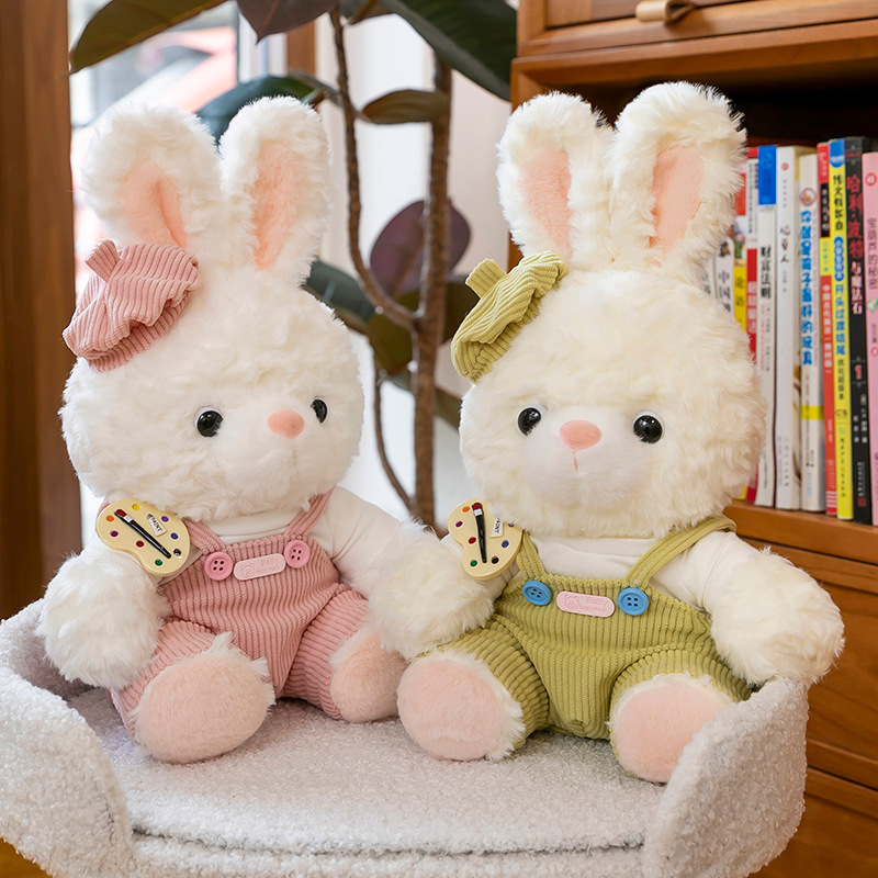Mora bunny plush toys in pink and green overalls sitting on a soft chair, warm home setting with bookshelf background