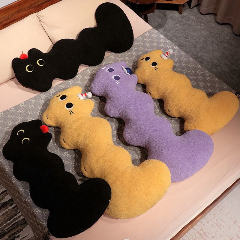 Cloud cat long plush pillow in black, yellow and purple, soft curved body cushions arranged on a bed highlighting elongated shape and playful cat details